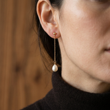 Boucles d'oreilles pendantes en or jaune 9 carats avec chaîne et perle blanche, portées à l'oreille.