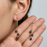 Boucles d'oreilles pendantes or jaune 9 carats et perles de culture noires de Tahiti portées à l'oreille.