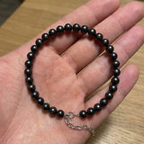 Bracelet en argent 925 avec perles noires 6/7 mm et fermoir réglable, présenté dans une main ouverte.