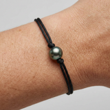 Bracelet homme en coton ciré noir avec perle de Tahiti verte porté au poignet.