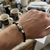 Bracelet homme en coton ciré noir avec perle de Tahiti et perles argent, porté au poignet.