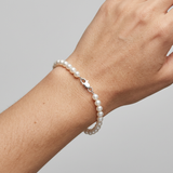 Bracelet en or blanc 9 carats et perles blanches porté au poignet, fermoir mousqueton argenté.