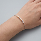 Bracelet or blanc 9 carats porté au poignet, orné de perles multicolores blanches, roses et grises.