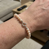 Bracelet en or blanc 9 carats et perles roses porté au poignet, fermoir anneau visible.