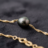 Gros plan sur la perle de Tahiti noire d'un bracelet chaîne torsadée en or jaune 9 carats.