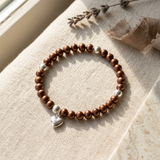 Bracelet perles d'eau douce chocolat argent 925 avec charm cœur, posé sur tissu beige.