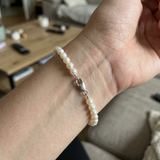 Bracelet perles blanches en or blanc 9 carats porté au poignet, fermoir mousqueton argenté visible.