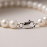 Gros plan sur le fermoir mousqueton en argent 925 d'un bracelet de perles blanches.