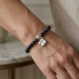 Bracelet perles d'eau douce noires porté au poignet avec charm trèfle en argent 925.