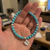 Bracelet perles d'eau douce turquoise argent 925 avec pendentif trèfle, tenu dans une main.