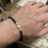 Bracelet perles noires 5/6 mm en argent 925 avec fermoir mousqueton porté au poignet.