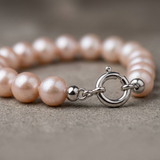 Bracelet perles roses avec fermoir anneau ressort en or blanc 9 carats posé à plat.