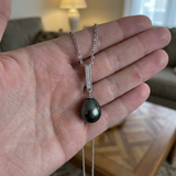 Collier argent 925 avec pendentif barre pavée et perle noire de Tahiti, tenu dans une main.