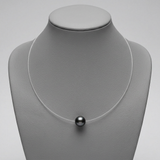Collier argent 925 fil transparent avec une perle noire de Tahiti, présenté sur buste.