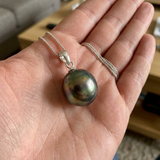 Collier argent 925 avec perle de Tahiti cercle 11-12 mm aux reflets verts, tenu dans une main.
