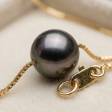 Gros plan sur la perle de Tahiti noire du collier en or jaune 9 carats et son fermoir.