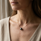 Collier en or jaune 9 carats avec perle de Tahiti noire porté au cou.