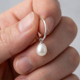 Boucle d'oreille créole argent 925 avec perle de culture blanche en forme de goutte, tenue en main.