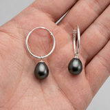 Boucles d'oreilles créoles argent 925 avec perles de culture noires de Tahiti, posées dans une paume.