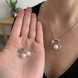 Collier cœur et boucles d'oreilles puces à perle blanche portés au cou et tenus en main.