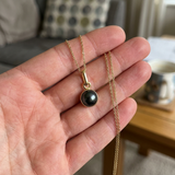 Pendentif or jaune 9 carats et perle de Tahiti noire présenté dans une main ouverte.